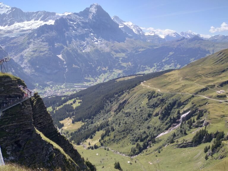 Scenic mountain hiking trail overlooking a green alpine valley and snow-capped mountains