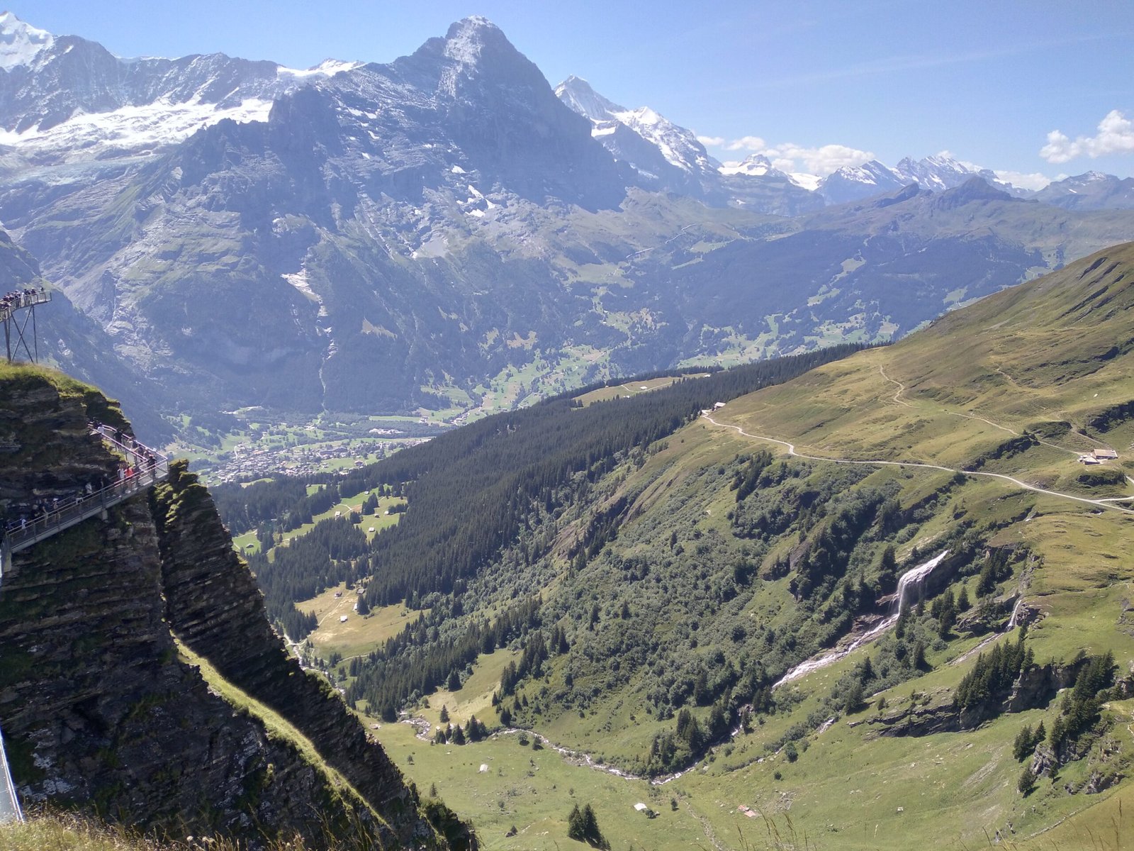 Scenic mountain hiking trail overlooking a green alpine valley and snow-capped mountains